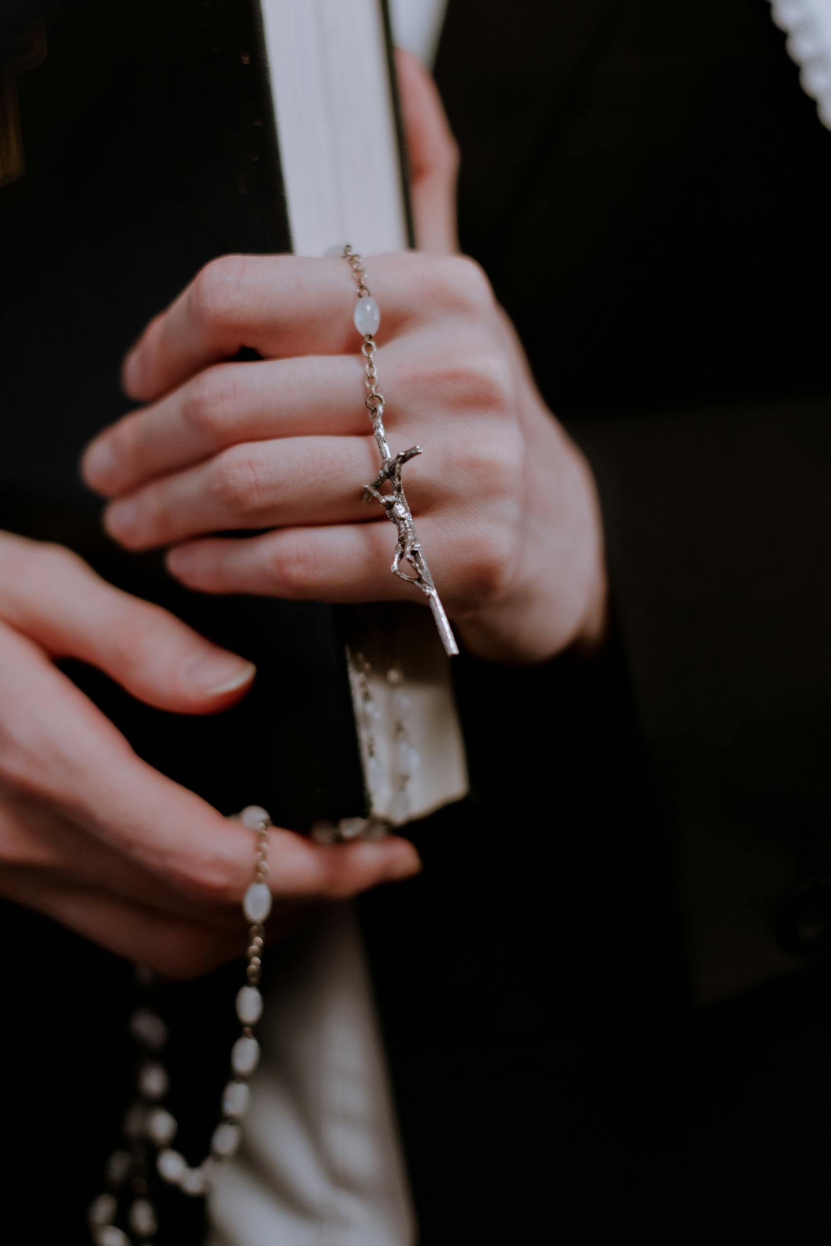 Close-up of female hands holding a rosary and a book, symbolizing faith and devotion.